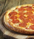 A whole pepperoni pizza lies on a wooden board on a wooden table Royalty Free Stock Photo