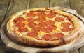 A whole pepperoni pizza lies on a wooden board on a wooden table Royalty Free Stock Photo