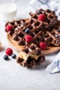 Whole and pieces chocolate waffles, glass of milk on a gray background