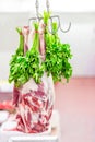 Whole raw lamb leg hanged on hook with bunch of parsley at market or shop. Meat prepared for cook Royalty Free Stock Photo