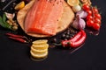 Whole red fish fillet on a wooden plate with cherry tomatoes, red and green chili peppers, black and green olives, lemon, garlic, Royalty Free Stock Photo