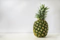 Whole ripe pineapple stands on a white surface with a light gray background