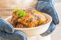 Whole roasted chicken in a baking bowl holding in hands cook with gloves