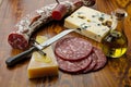 whole salami, olive oil bottle, cheese block, and pizza cutter on table