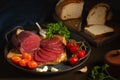 Whole and sliced bresaola on a metal round tray with tomatoes, garlic and bread