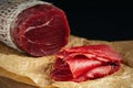 Whole and sliced bresaola on paper on a cutting board