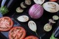 Whole and sliced eggplants and tomatoes on baking tray closeup