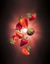 Whole and sliced fresh strawberries in the air with flash of light in the dark