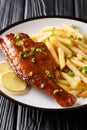 Whole spicy fried sea perch served with fresh lemon and French fries close-up in a plate. vertical