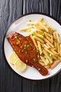 Whole spicy fried sea perch served with fresh lemon and French fries close-up in a plate. vertical top view