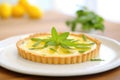 whole tarte au citron on a white plate, fresh mint leaf on top