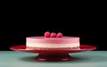 A whole three-layered raspberry cheesecake on a red cake stand topped with fresh berries on teal surface against minimalist black Royalty Free Stock Photo