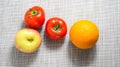 Whole tomatoes, apple and orange on a light surface