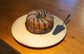 Whole uncut brown sugar coated Bundt cake on white turntable with silver cake shovel