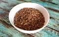 Whole unpeeled milk thistle seeds in a white bowl on an old shabby wooden background.