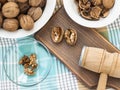Whole walnuts, shells and kernels in a bowls around a brown wooden board with cracked nuts and wooden meat mallet. Natural