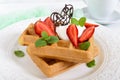 Whole wheat Belgian waffles with whipped cream, freshly chopped strawberries, mint leaves and chocolate and a cup of tea Royalty Free Stock Photo