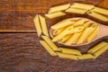 Wholemeal Pasta. Integral Penne into a brown bowl ith a wooden spoon over a wooden table Royalty Free Stock Photo
