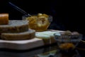 Wholewheat breads with cheese, jams and green olives on a wooden chopping board with their reflections, close up, macro