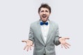 Why? what? Portrait of confused handsome bearded man in casual grey suit, blue bow tie standing and looking at camera with raised