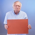 Why would they do that. Studio shot of a senior man holding a blank sign and looking unhappy against a blue background. Royalty Free Stock Photo