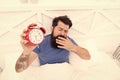 Why you suffering in mornings. Get up with alarm clock. Waking up early. Man bearded sleepy face bed with alarm clock in