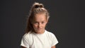 Wicked or malign little girl with pony tail hair looking at the camera wearing white t-shirt and black pants isolated on