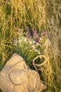 A wicker bag made of straw and a bouquet of wildflowers in the grass.