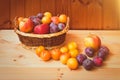 Wicker basket with apples and colorful plums on wooden table. Royalty Free Stock Photo