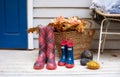 Wicker basket with autumn leaves, pumpkin and rubber boots to contryyard of house. Red checkered and blue rain boots in front of h