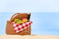 Wicker basket with blanket, bottle of wine and fruits near sea. Beach picnic Royalty Free Stock Photo