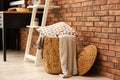 Wicker basket with blankets and pillow near wall, space for text. Idea for interior design