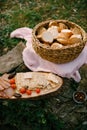 Wicker basket of bread on a bed on the ground with a wooden stand and biscuit biscuits, tomatoes and ham on it.