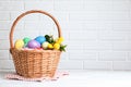 Wicker basket with bright painted Easter eggs and spring flowers on white wooden table near brick wall. Space for text Royalty Free Stock Photo