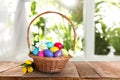 Wicker basket with bright painted Easter eggs and spring flowers on wooden table Royalty Free Stock Photo