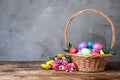 Wicker basket with bright painted Easter eggs and spring flowers on wooden table against grey background. Space for text Royalty Free Stock Photo