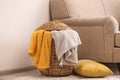 Wicker basket with color blankets and pillow near sofa, space for text. Idea for interior design