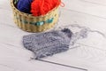 Wicker basket with colorful knitting yarns, knitting needles and knitting on white wooden table