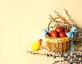 Wicker basket decorated with blue ribbons with Easter brown eggs, willow twigs and a lovebird parrot in bright festive yellow and