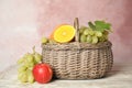 Wicker basket with different fruits on white wooden table near pink wall Royalty Free Stock Photo