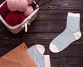 Wicker basket filled with wool and yarn with striped white socks on a dark wooden background