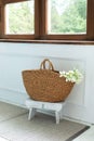 Wicker basket with flowers and wooden stool near window. Living room hygge, home decor. Scandinavian interior. Rustic at home. Royalty Free Stock Photo