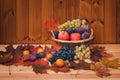 Wicker basket with fresh fruits and autumn maple leaves on wooden background. Royalty Free Stock Photo