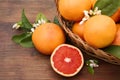 Wicker basket with fresh grapefruits and green leaves on wooden table