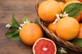 Wicker basket with fresh grapefruits and green leaves on wooden table