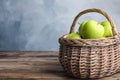 Wicker basket of fresh ripe green apples on wooden table against blue background Royalty Free Stock Photo