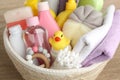Wicker basket full of different baby cosmetic products, bathing accessories and toys on wooden table, closeup