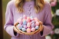 A wicker basket full of painted pastel colors Easter eggs in the hands of a woman in purple sweater