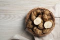 Wicker basket with many Jerusalem artichokes on white wooden table, top view. Space for text Royalty Free Stock Photo