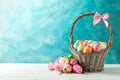 Wicker basket with painted Easter eggs and flowers on table against color background Royalty Free Stock Photo